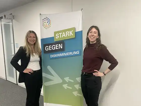 Sarah Perry mit einer Kollegin neben dem Roll-up „Stark gegen Diskriminierung“