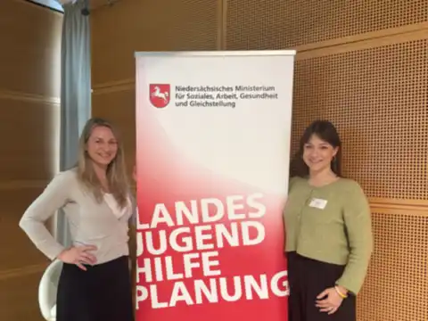 Sarah Perry mit einer Kollegin neben dem Roll-up „Landesjugendhilfeplanung“ des Niedersächsischen Sozialministeriums